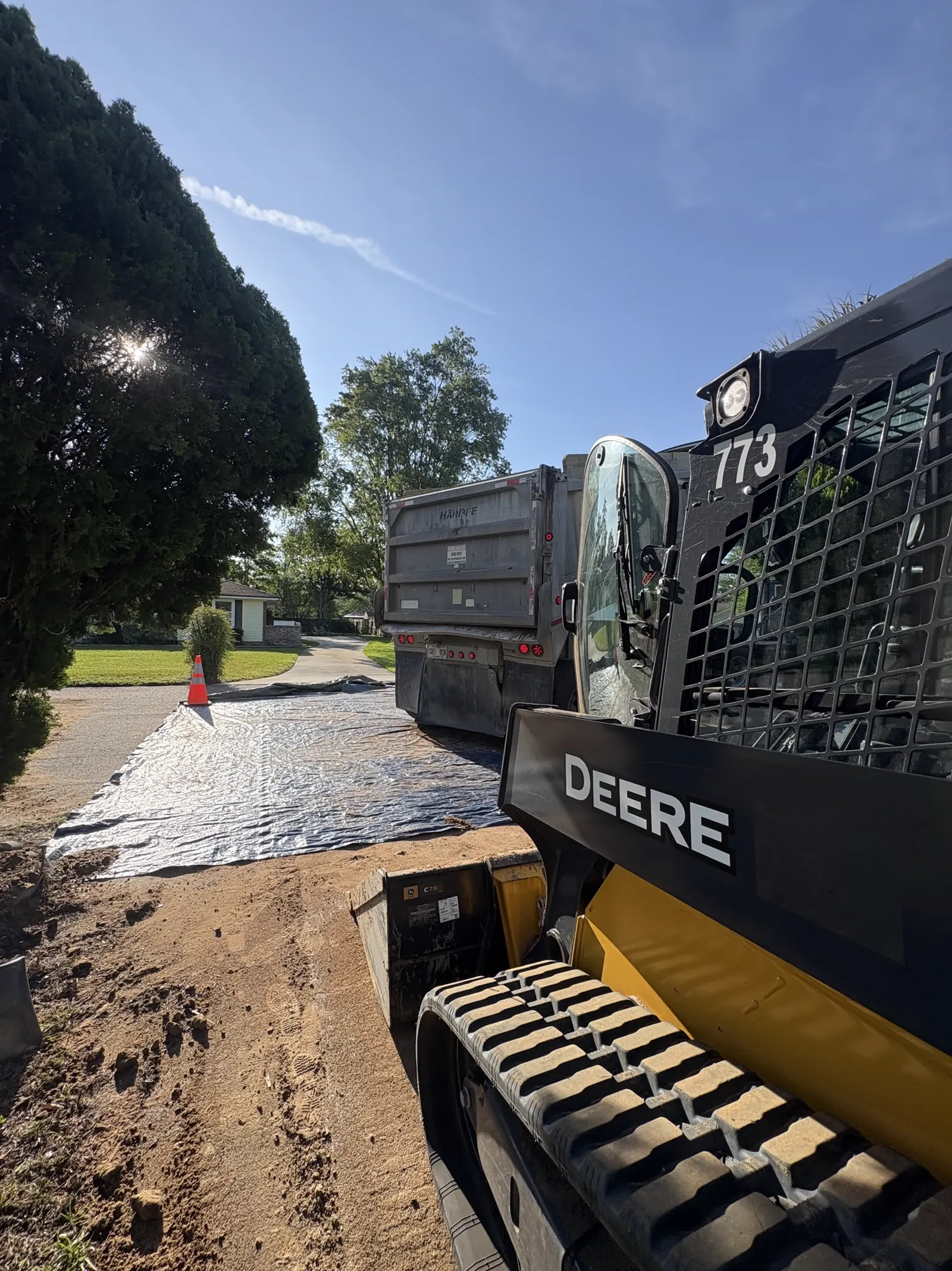 John Deere 325 skid steer and dump truck staging fill dirt at the street on a tarp for a tight-access pool fill-in in NE Middleburg FL